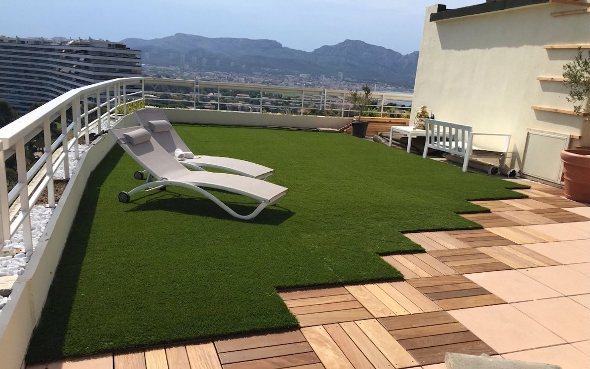 Toit-terrasse aménagé : gazon synthétique, caillebotis bois et bains de soleil face à la mer — Marseille